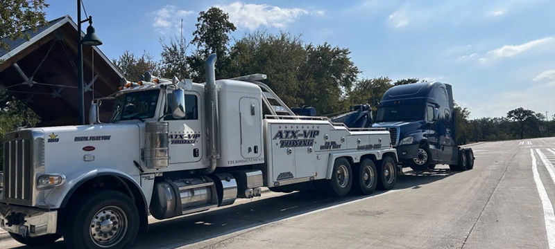 Heavy-duty wrecker towing dark blue semi truck in Mustang Ridge TX