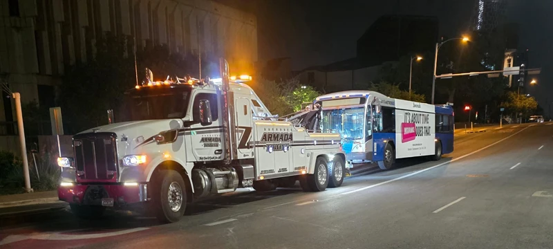Heavy-duty tow truck towing a transit bus at night in Mustang Ridge